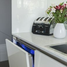 Built-in dishwasher under white granite top with toaster and vase of flowers