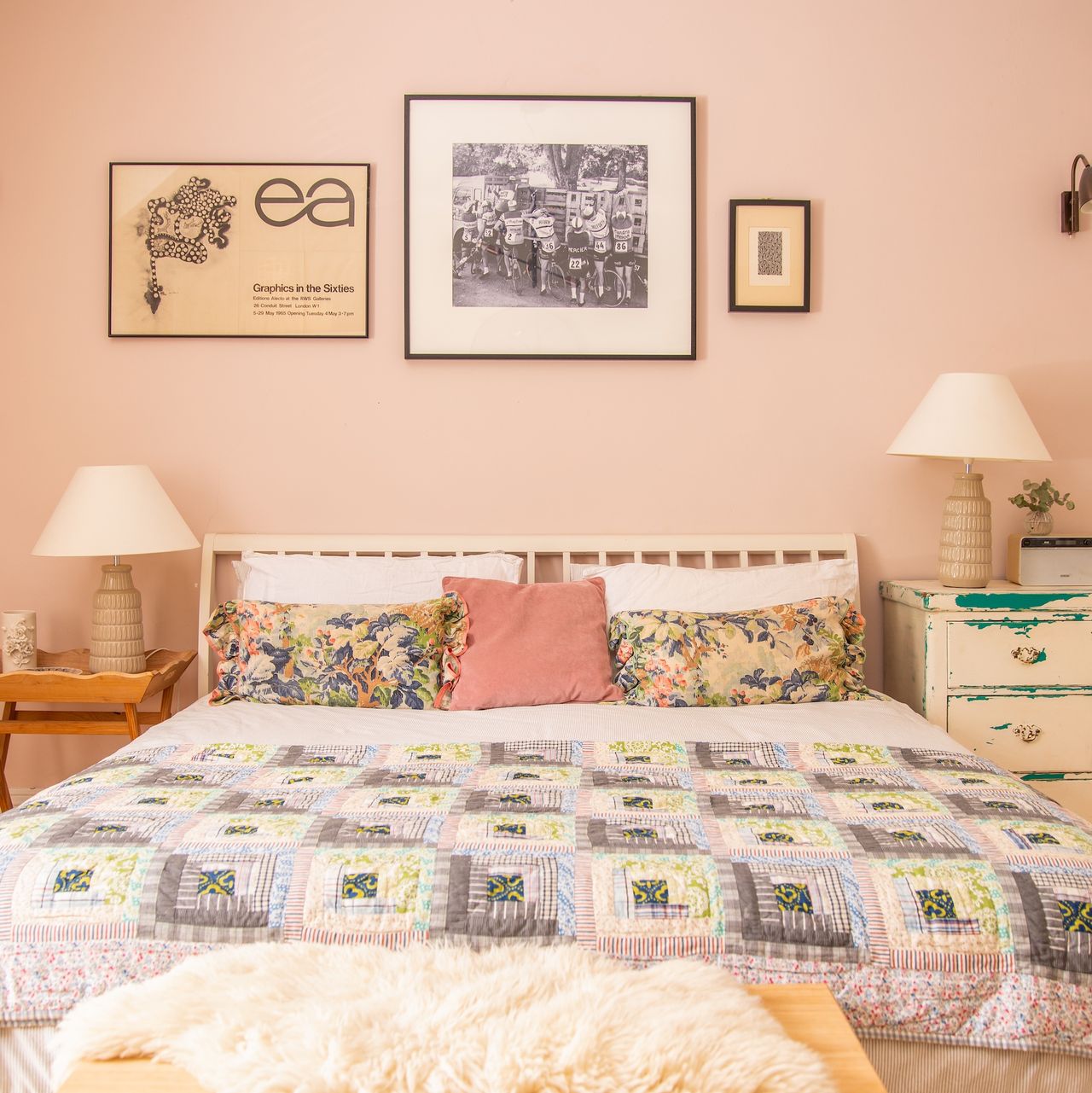 bedroom with pink painted walls and double bed with patchwork quilt, with lamps on either side and photographs hung on wall above bed