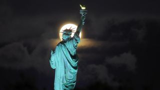 Полная голубая луна осетра восходит за факелом Статуи Свободы в Нью-Йорке 22 августа 2021 года, если смотреть из Джерси-Сити, штат Нью-Джерси.
