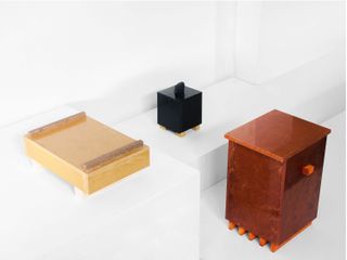 3 wooden objects in different colours displayed on white surface photographed against white wall