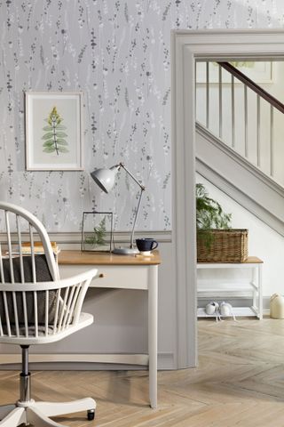 Slate grey floral wallpaper by John Lewis & Partners with wood and white desk, white painted wooden chair and hallway in background