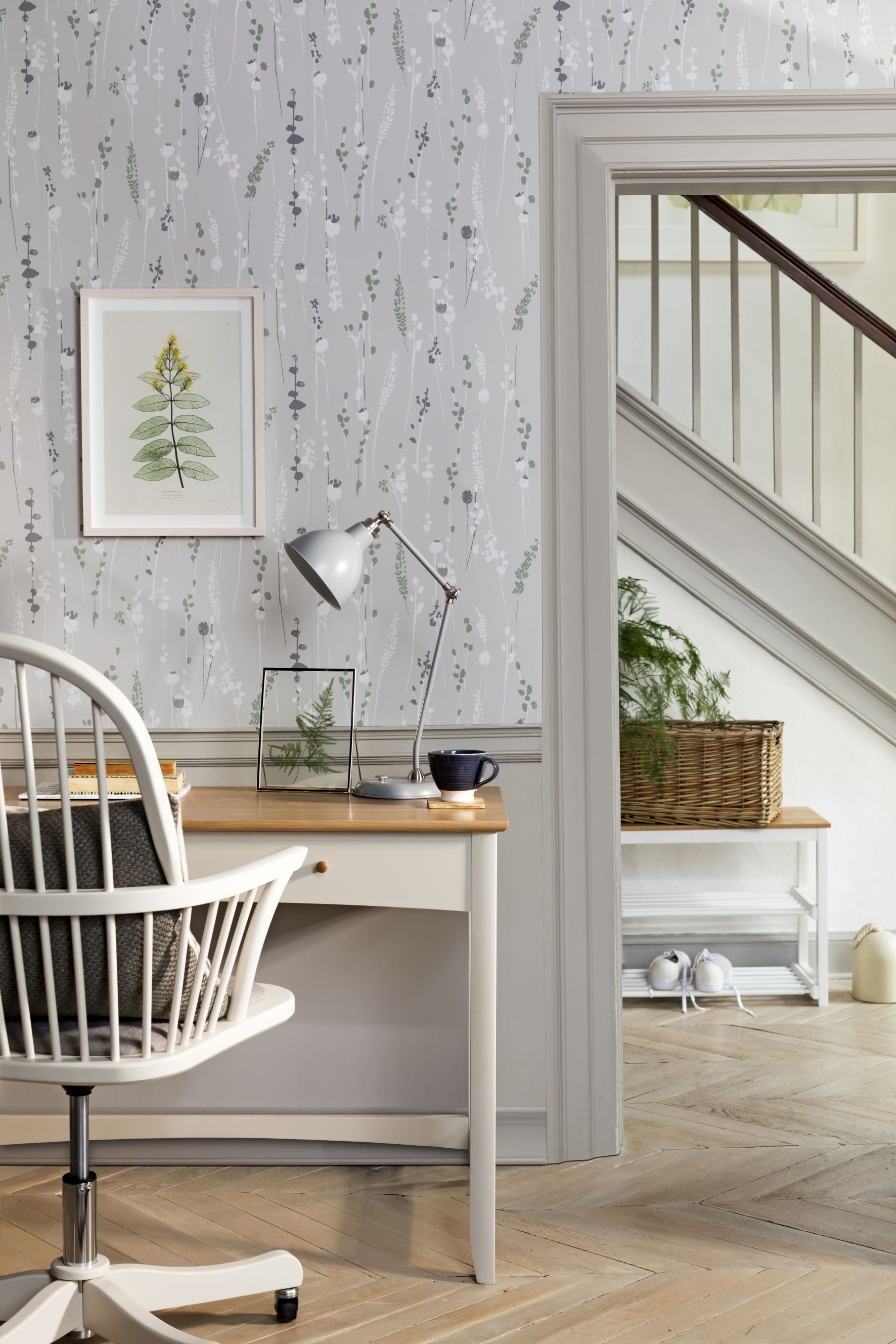 Slate grey floral wallpaper by John Lewis & Partners with wood and white desk, white painted wooden chair and hallway in background