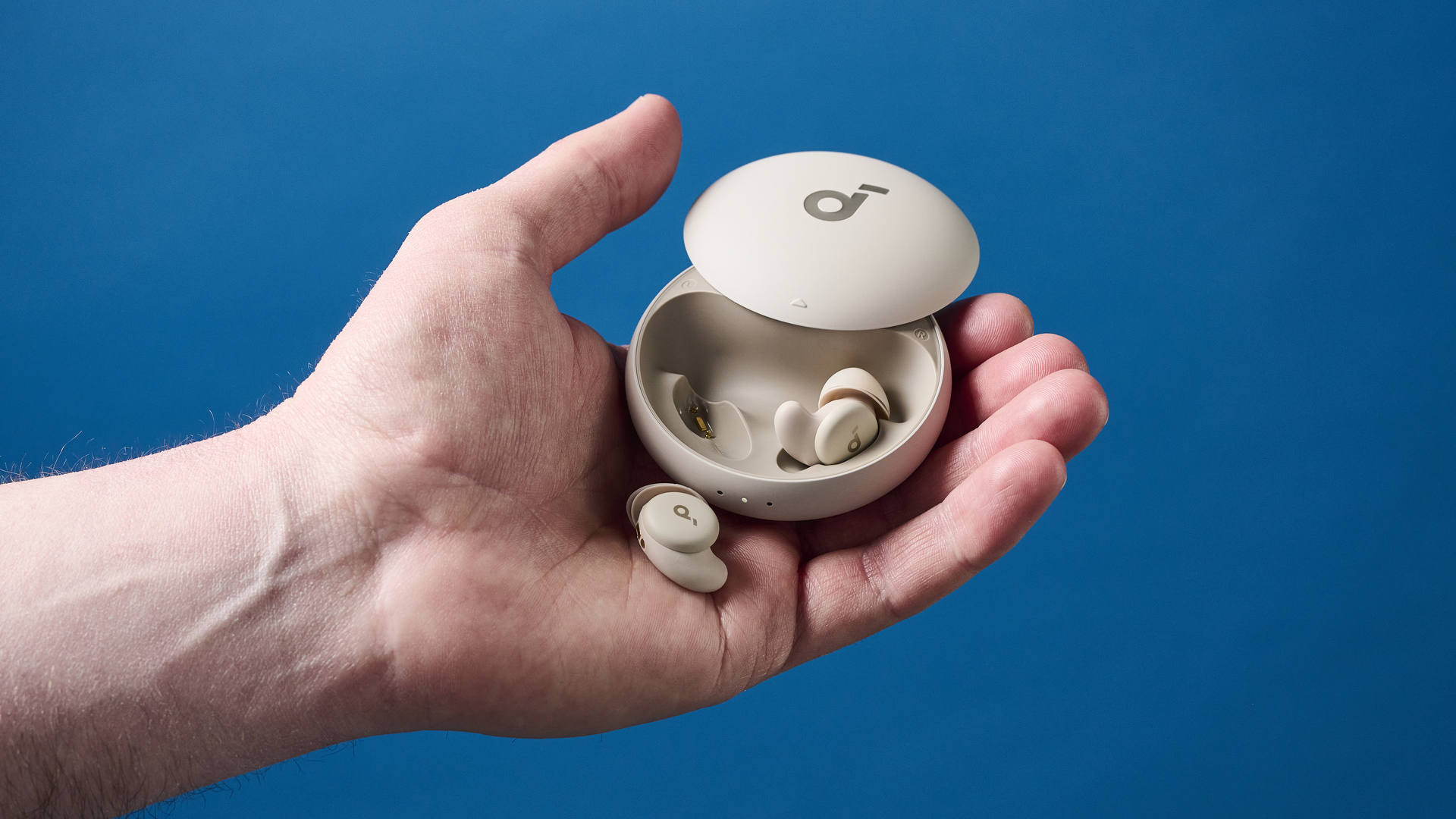 A photo of the Soundcore Sleep A20 earbuds in their open case being held in hand with a blue wall in the background.