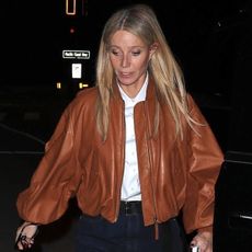 Gwyneth paltrow wears a tan leather jacket and white top with jeans.