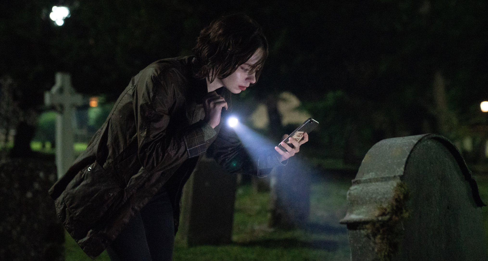emma myers as pip shining a flashlight on a grave and looking at her phone in a good girl's guide to murder season 3