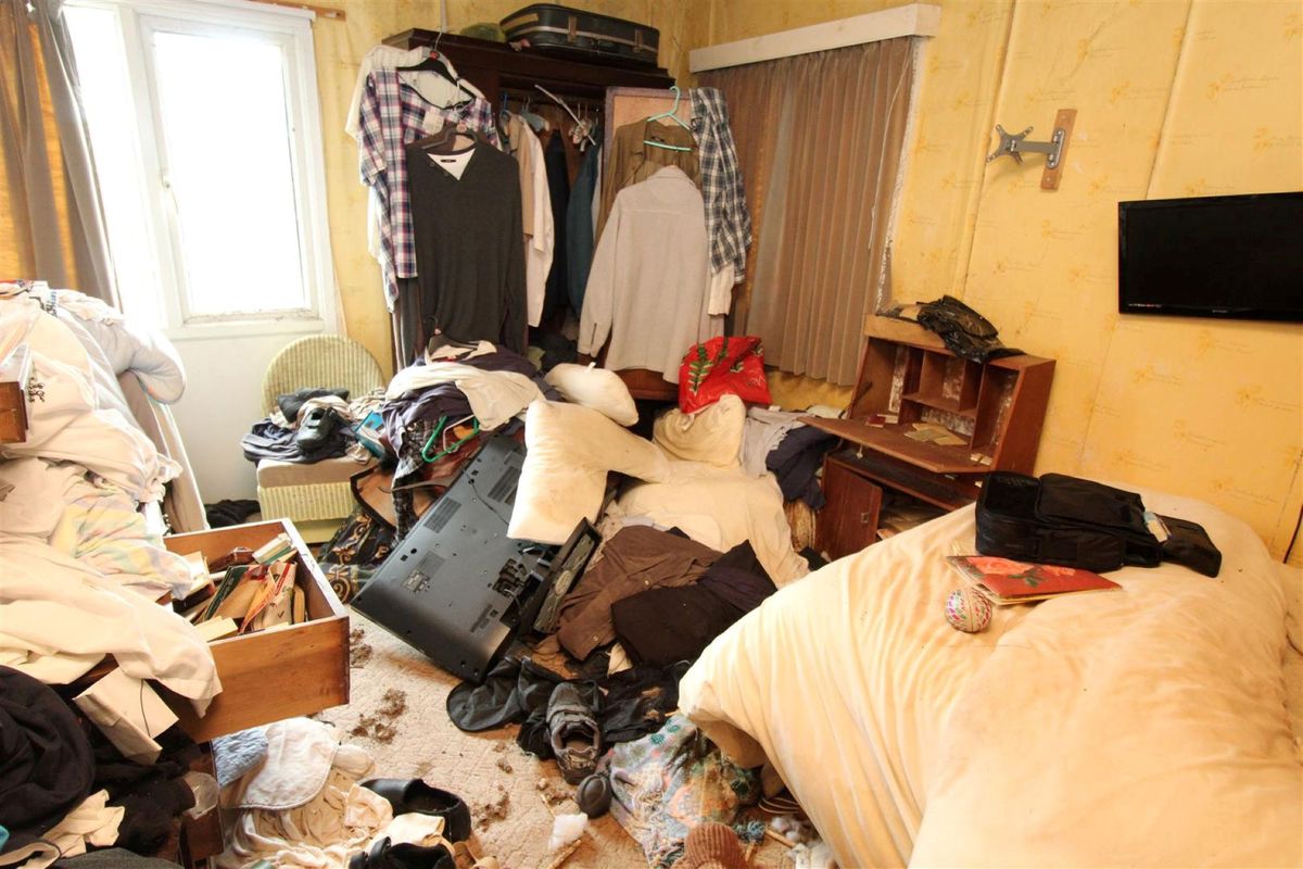 Another bedroom has clothes stacked high and a dirty carpet and an old tv on the floor