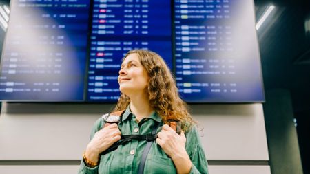 woman in front of flight board at airport 