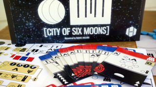 The box of City of Six Moons in from of its cards, laid out on a wooden surface