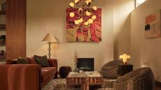 A living room with warm white plaster walls, a red abstract artwork on the wall, a brick red modern sofa, two pattern low armchairs, and a low-form coffee table. 