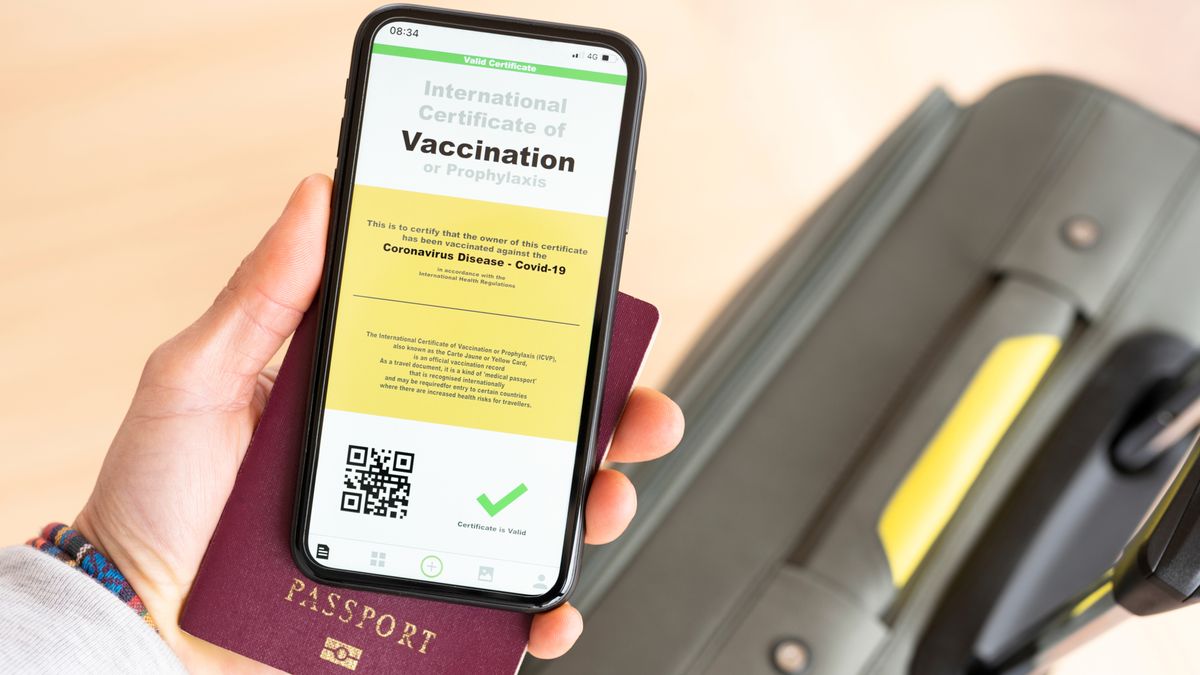 Overhead view of an human hand holding a passport and a smart phone with a digital illustration of a certificate of vaccination against the Covid-19 disease.