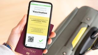 Overhead view of an human hand holding a passport and a smart phone with a digital illustration of a certificate of vaccination against the Covid-19 disease.