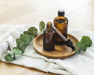 Brown amber glass bottle dropper with cosmetic oil with eucalyptus leaves on wooden plate