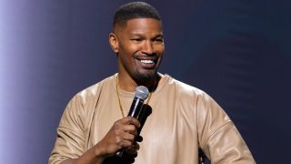 Jamie Foxx smiling and holding up a mic with his left hand in his 2024 stand up special.