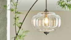 Outdoor Eloise ceiling light by Anthropologie hanging in a white plaster patio area with leafy trees