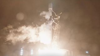 a tall white rocket lifts off into the night sky, its bright white engine plume lighting the area below