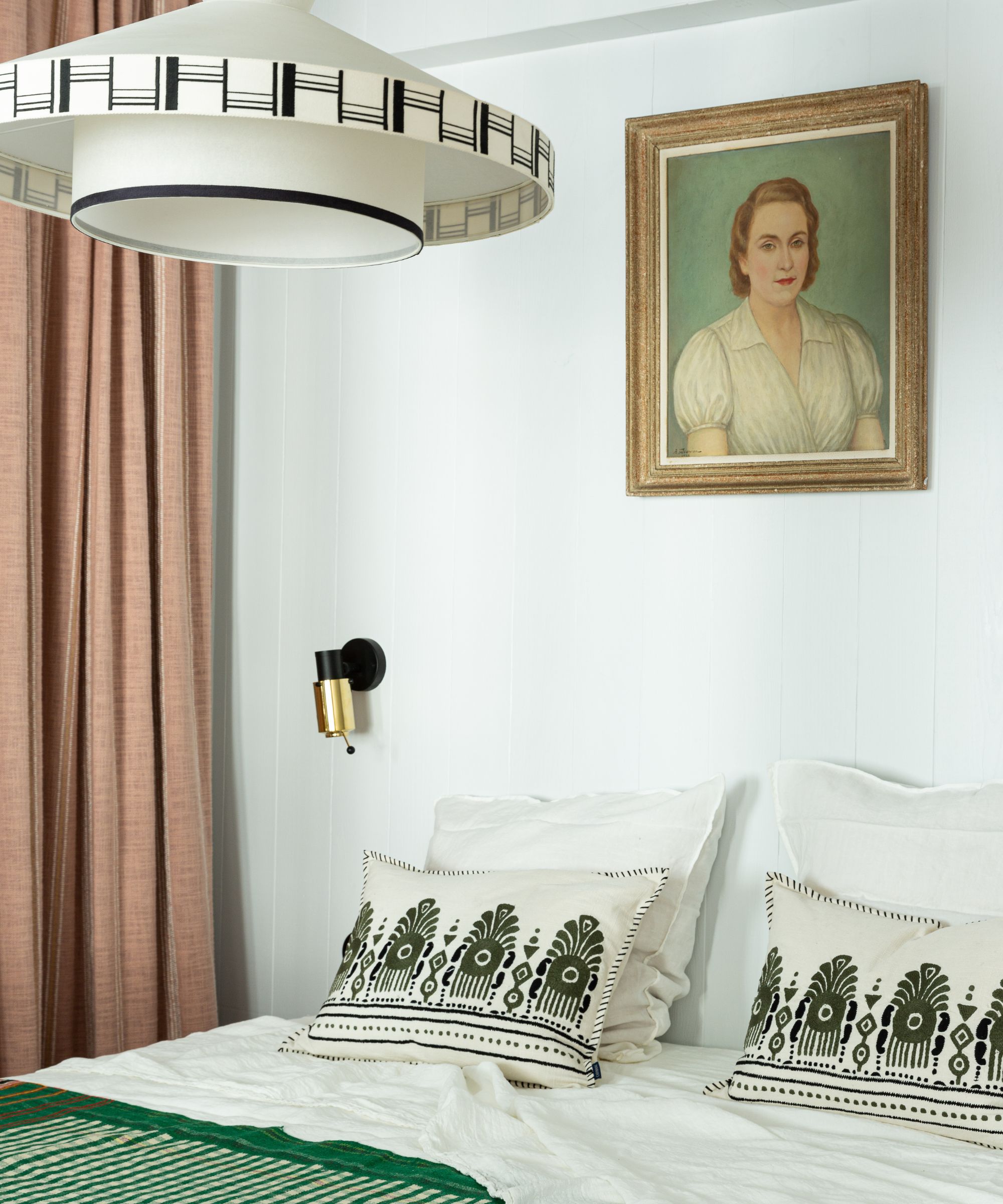 Bedroom with linen bedding and green throw, gold sconce, vintage portrait on wall and Art Deco light