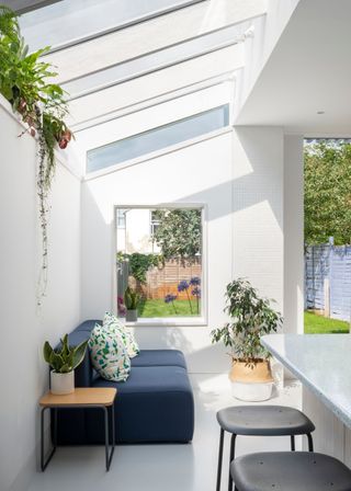 A kitchen with skylights and a window looking onto the garden. In the kitchen is a navy blue sofa with potted plants placed next to it