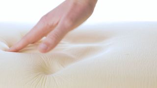 Image shows a hand pressing down into a memory foam mattress