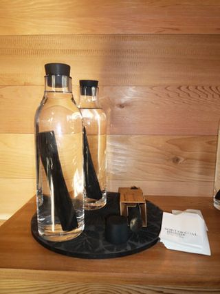Two clear glass bottles filled with water and a block of charcoal. Photographed on a black round tray placed on a brown wooden surface