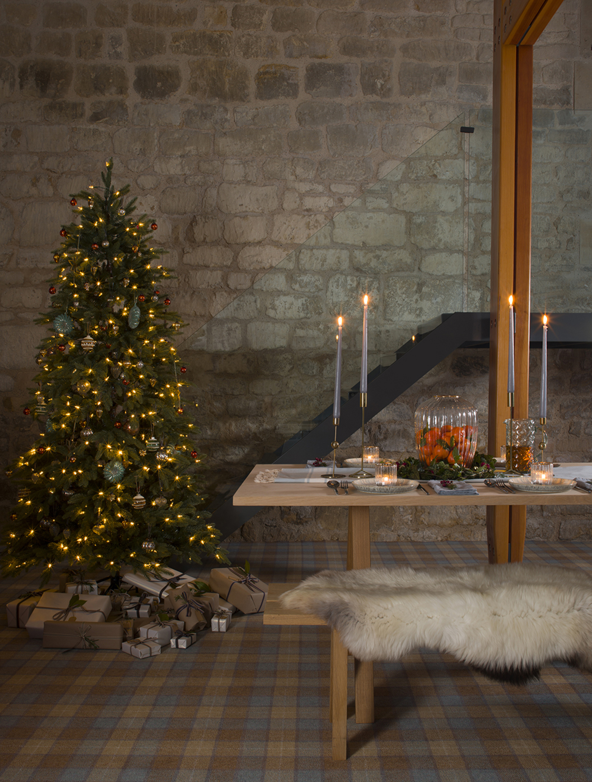 A dining bench decorated for Christmas with a fur blanket on the beat seat and a Christmas tree in the corner