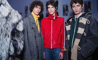 Three models stood looking at the camera - two in grey coats and one in red jacket