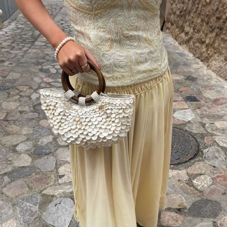 Creator @michellerosedrumm on holiday wearing a floaty skirt and holding a shell-inspired bag