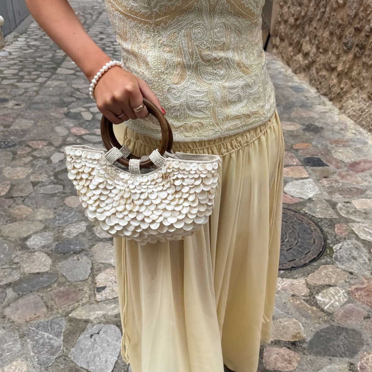 Creator @michellerosedrumm on holiday wearing a floaty skirt and holding a shell-inspired bag