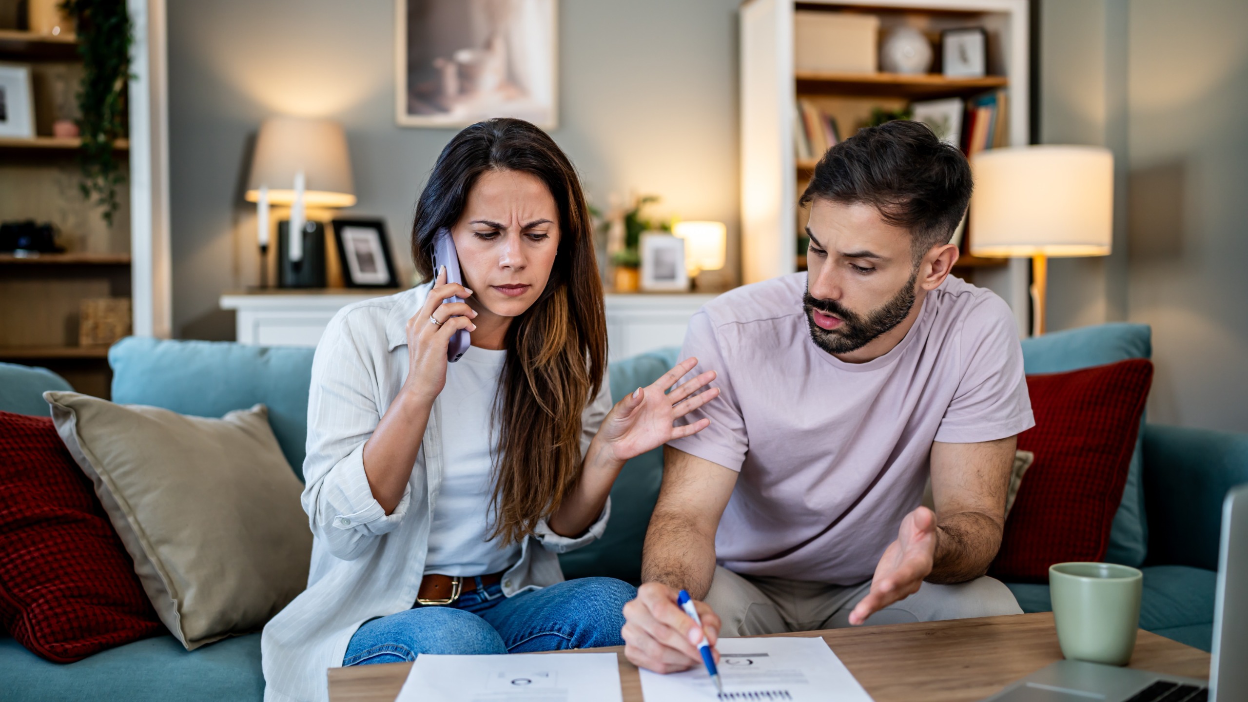 A young couple sitting on their couch looking stressed while talking about money.