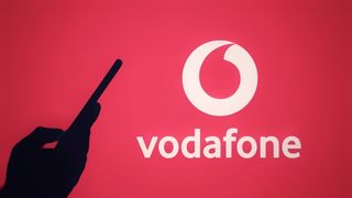 The silhouette of a hand holding a mobile phone in front of the Vodafone logo