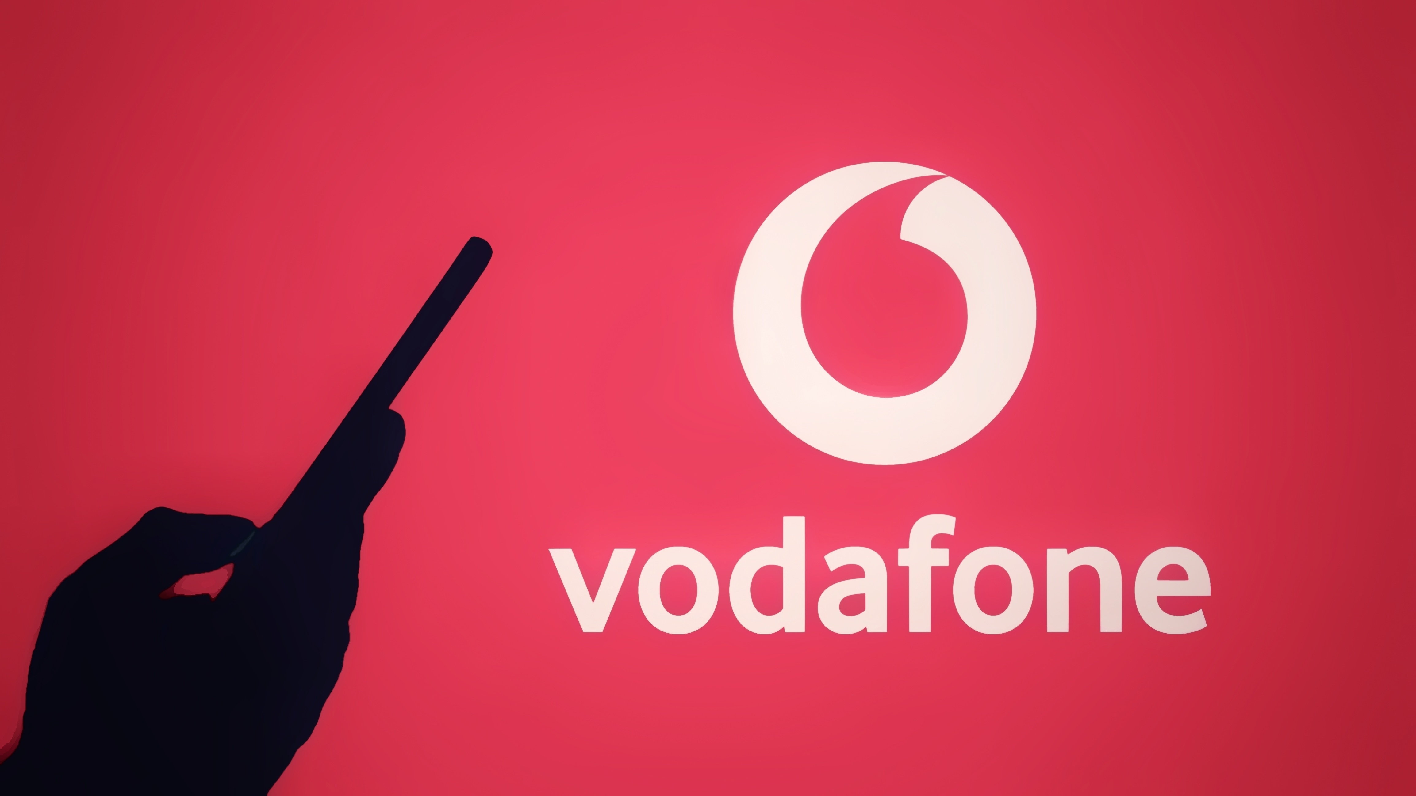 The silhouette of a hand holding a mobile phone in front of the Vodafone logo