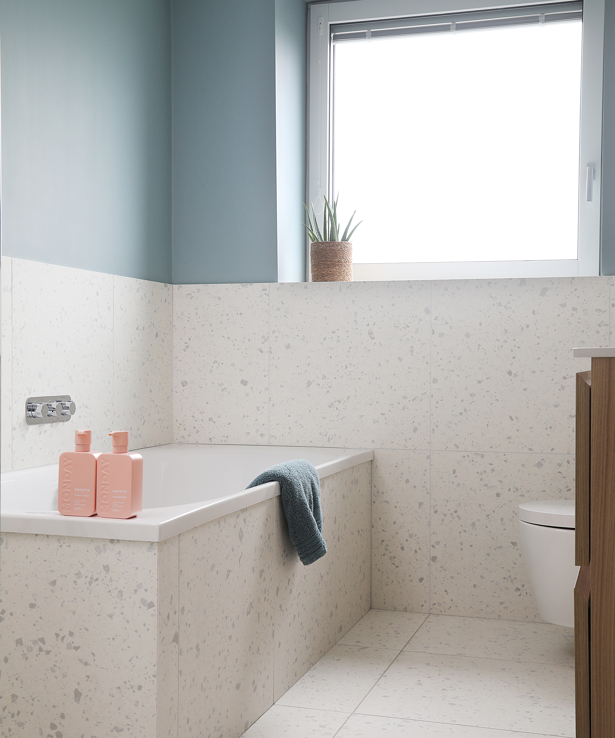 A small bathroom with bath painted blue with light terrazzo tiling 