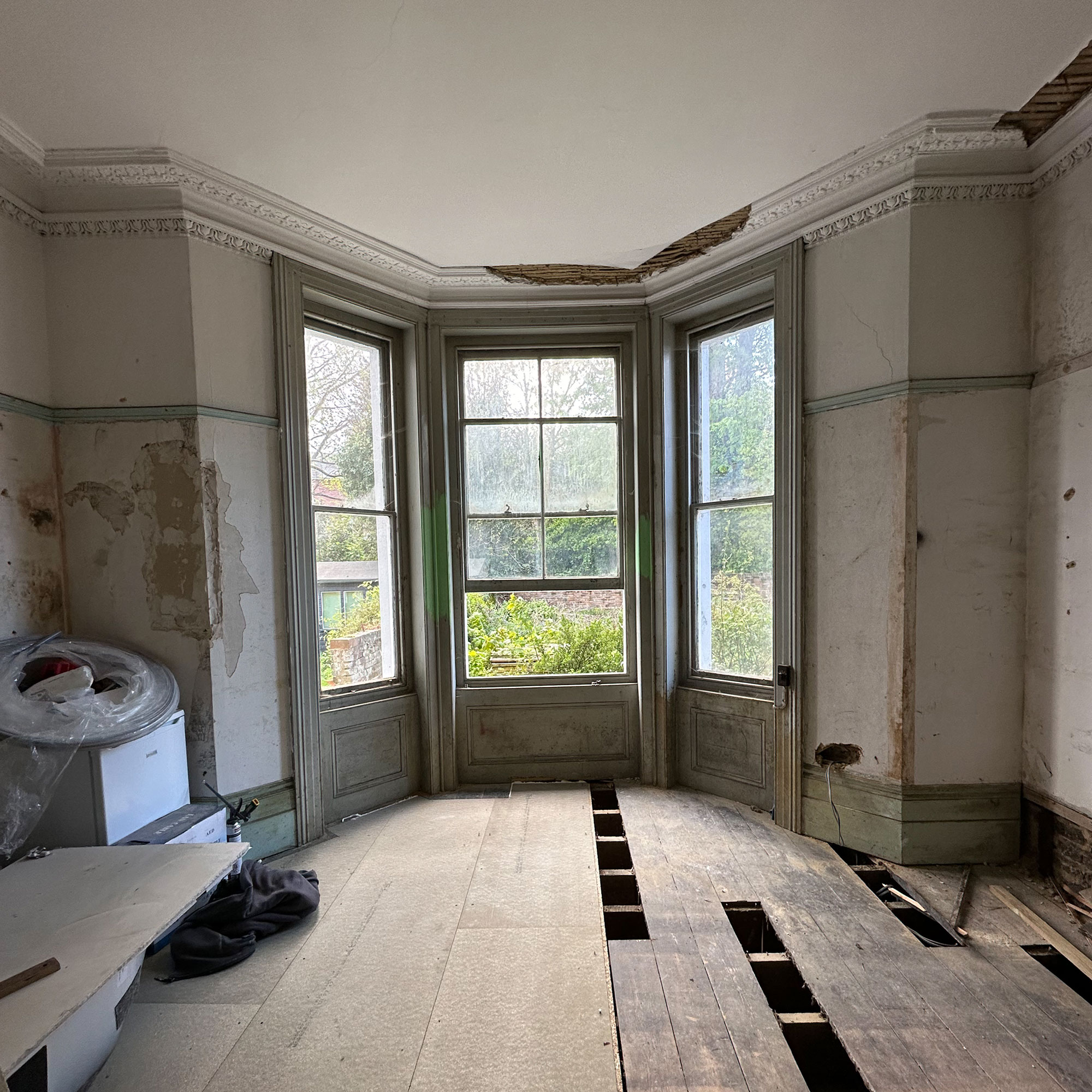 Bare room with bay window, stripped walls and wooden floors mid-renovation