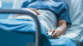 Photo of a man laying on an elevated hospital bed with a oxygen monitor on his finger