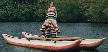 Model wearing a colourful dress from net-a-porter standing on canoes in a tropical river