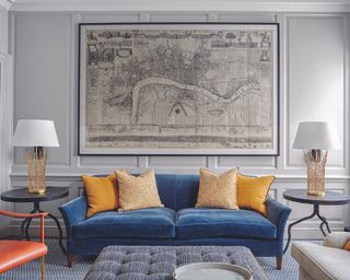 A grey living room with blue velvet sofa and large framed map print.