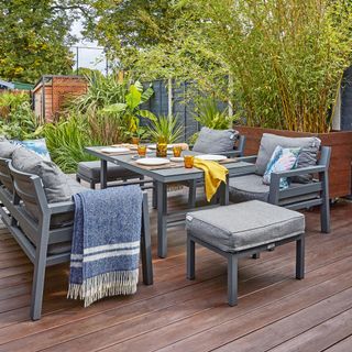 Grey outside dining area with table, sofa, chairs and stools on wooden deck area