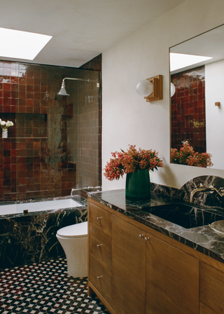 Burgundy tiles around a bathtub with black marble sides and a black and white tiled floor