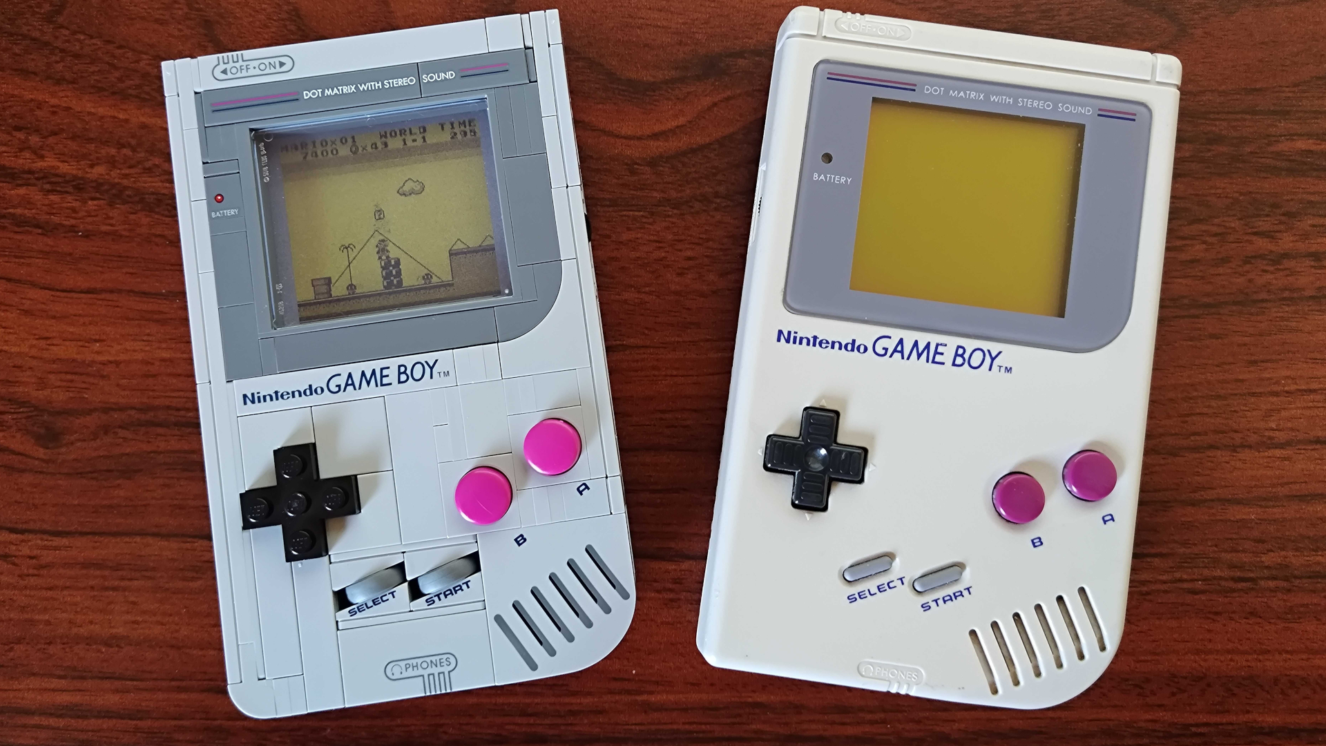 A Lego Game Boy beside an actual Game Boy console on a wooden surface
