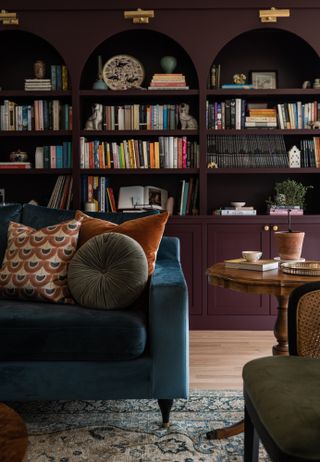 Dark blue velvet sofa with square and round cushions in front of floor-to-ceiling bookshelves