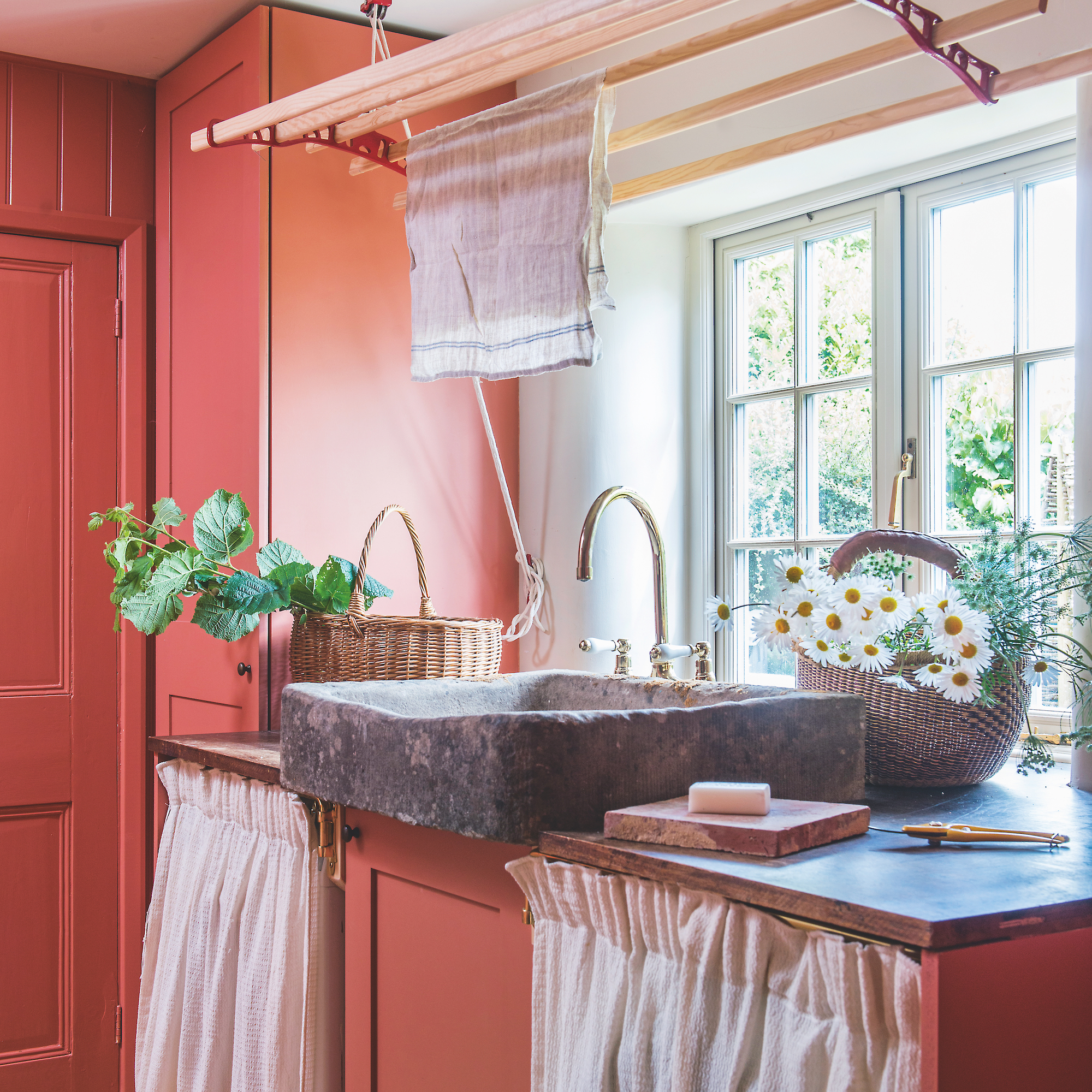 small utility room painted in terracotta red with stone sink and curtain cupboard covers