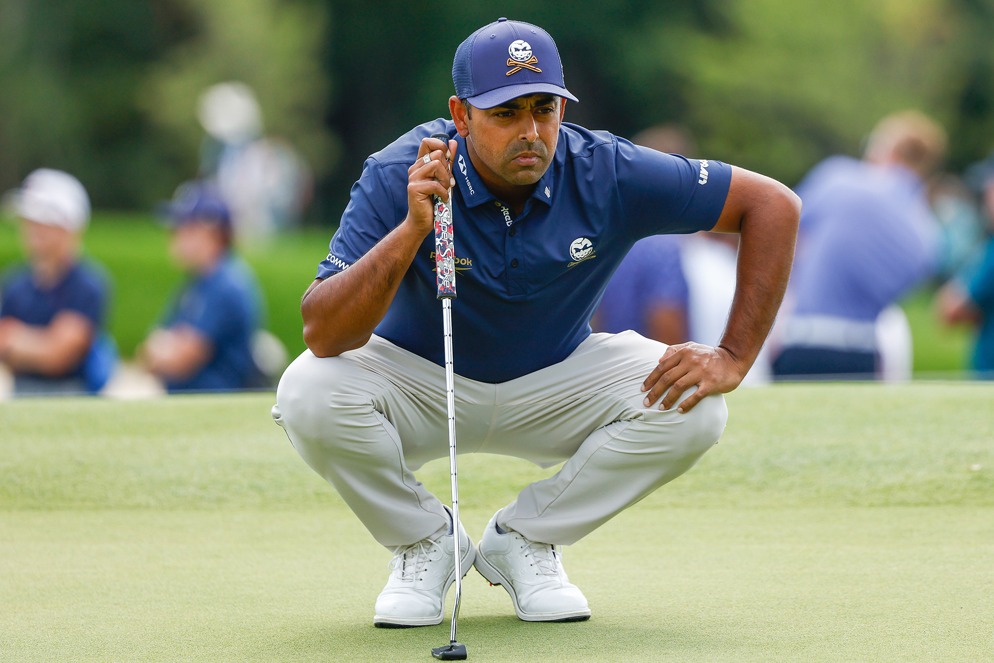 Anirban Lahiri crouching down to read a putt on the green, using his putter for balance as he looks a the line of his putt
