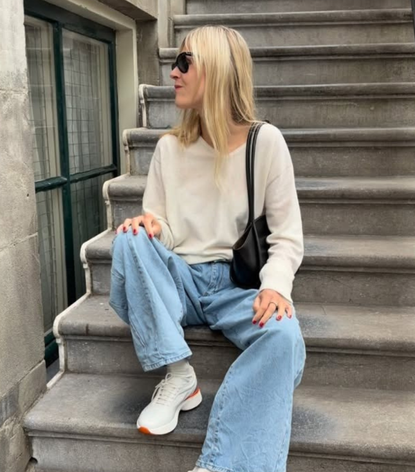 a woman wearing a cream sweater, blue jeans, and chunky jeans