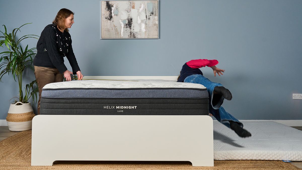 Mattress tester Nicola Appleton rolls of the side of the Helix Midnight Luxe mattress in our Sleep Studio, as she tests the edge support. Tester Ruth Jones stands on the other side of the other side of the mattress, measuring the space on the surface