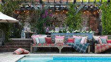 poolside tablescape sat under a pergola with a rustic bench seat with plaid and floral pillows, blankets and a patio umbrella