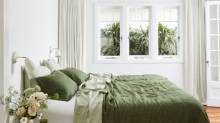 a neutral bedroom with green bedding and pillows on top. The bed overlooks a bright window looking into the garden.