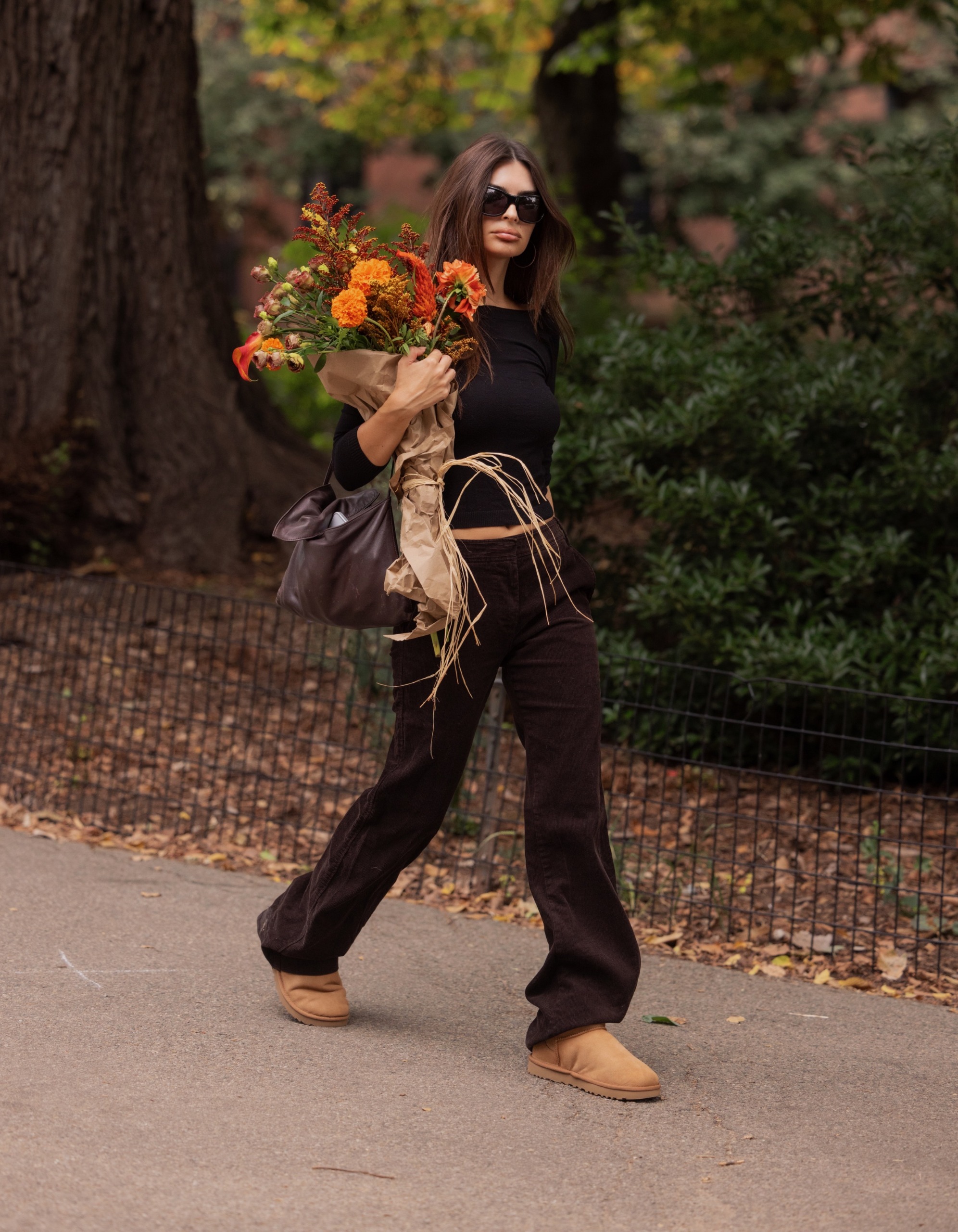 Emily Ratajkowski wears a long-sleeve shirt, dark brown jeans, Ugg boots, and a brown leather bag.