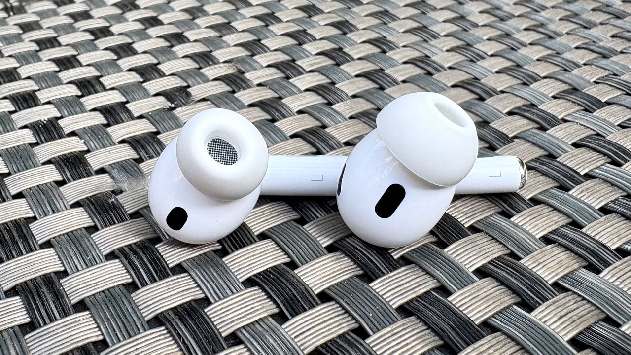 Apple AirPods Pro 3 either worn by a man standing in front of a red-brick wall, or on a table with gray twine cover