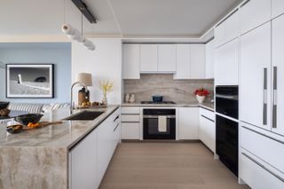 A kitchen with white cabinets, and light wood flooring