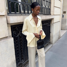 An image of an influencer wearing a shirt trend for 2026, a satin button-down in a butter yellow hue with cream silk trousers and holding a small handbag