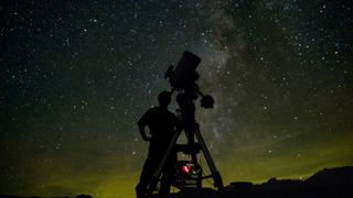 a silhouette of a person looking up through a telescope under a starry night sky 